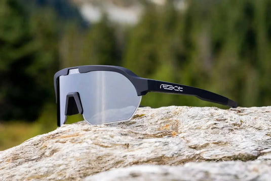 REACT Sunglasses Optray with adaptive lenses and solar-powered frame on a rock outdoors.